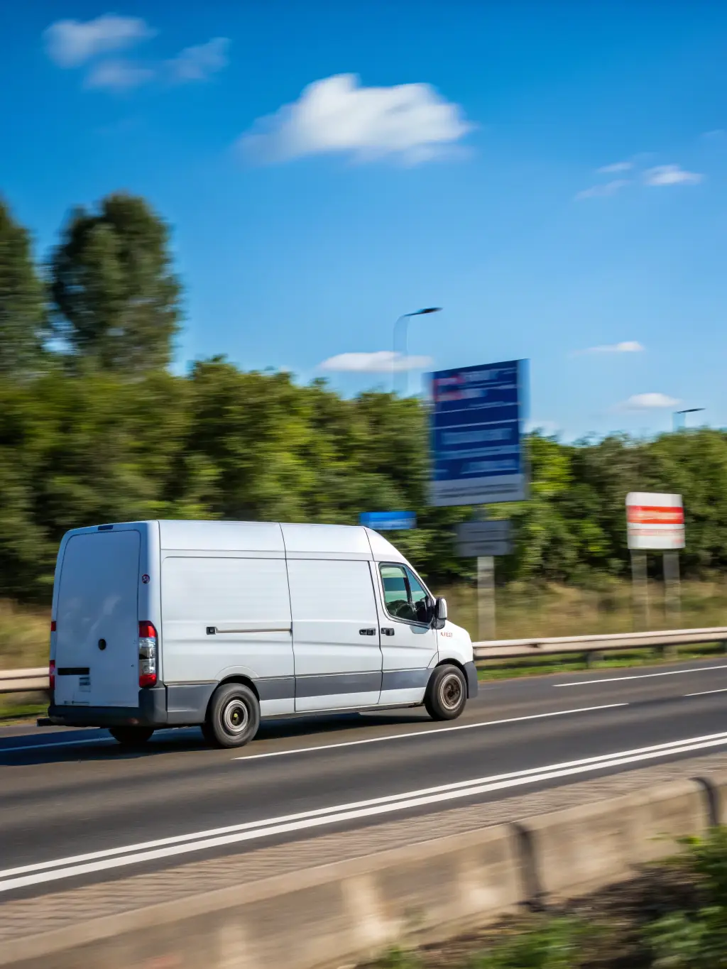 A delivery van speeding down a UK motorway, with a blurred background to emphasize motion and urgency, under a clear blue sky.